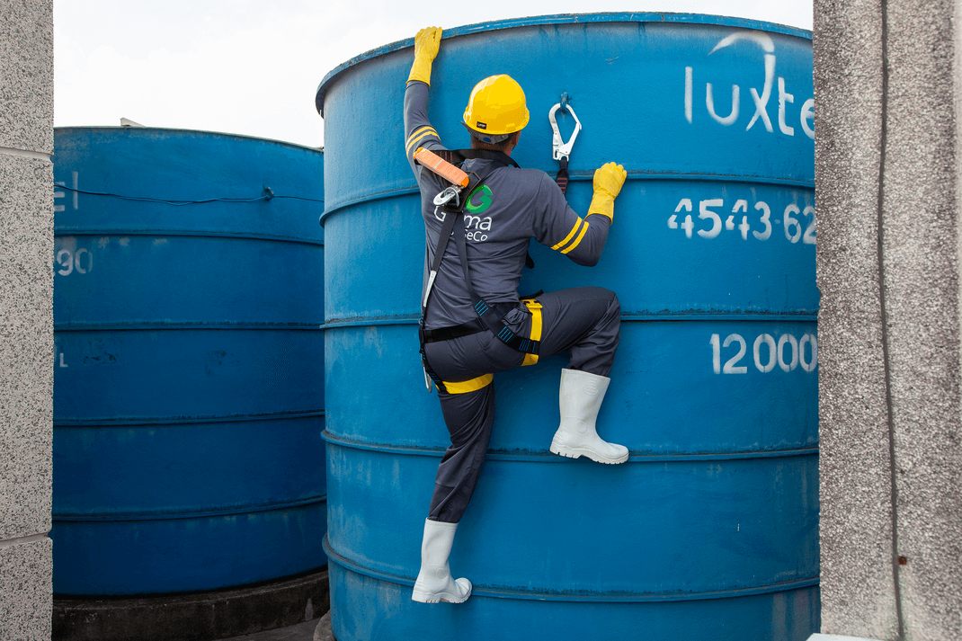 Técnico de manutenção escalando tanque de armazenamento em instalações industriais.